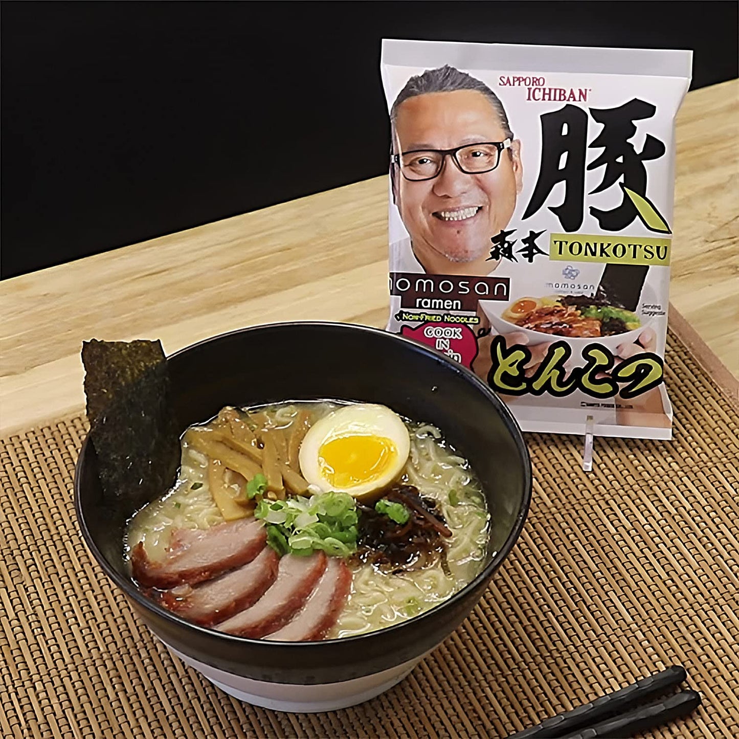 Bowl of ramen with a package of Sapporo Ichiban Tonkotsu ramen on a wooden surface.